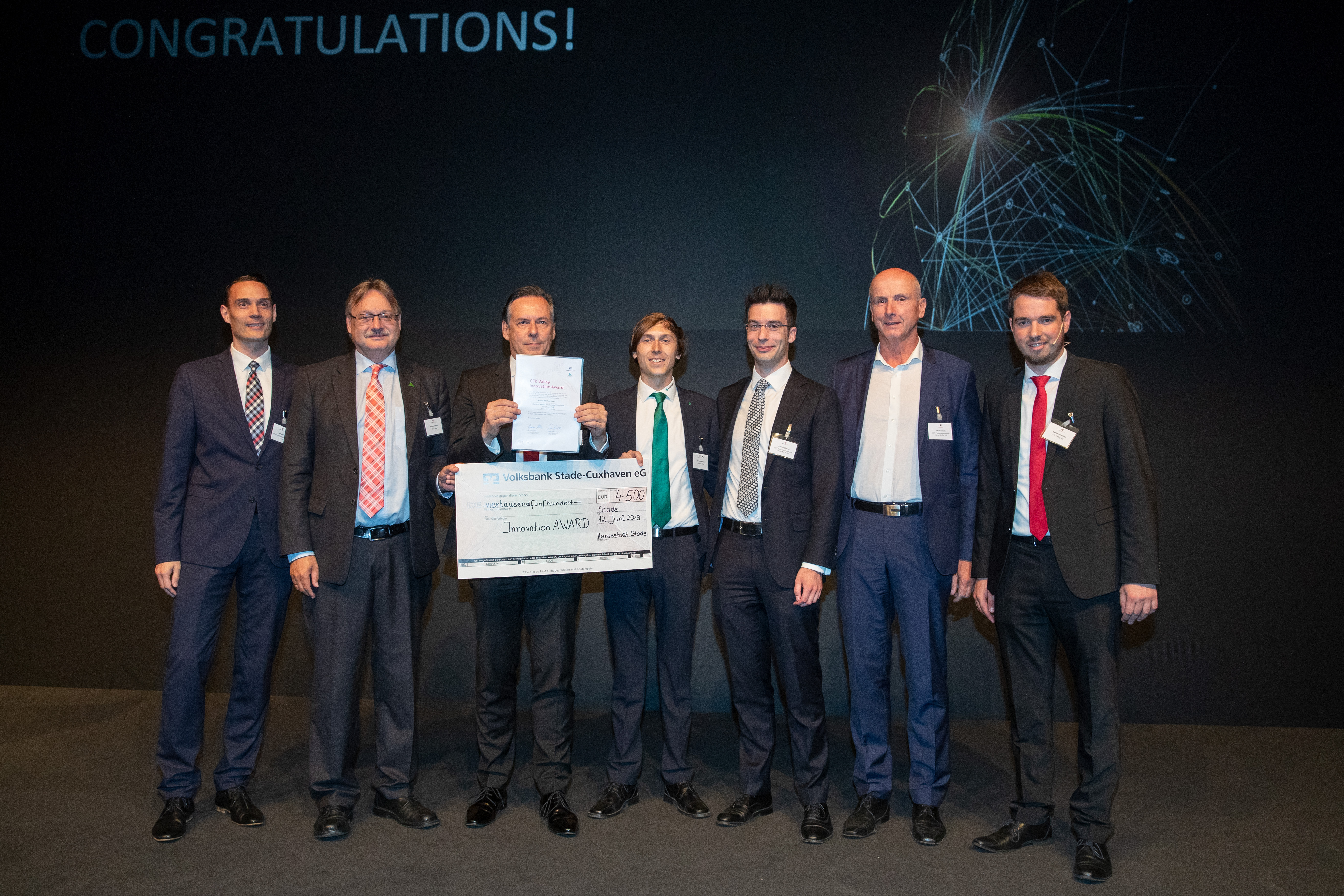 Christoph Brillinger vom Fraunhofer IFAM Stade (Mitte) empfängt für das MBFast18-Projekt die CFK Valley Innovation Award 2019-Urkunde und das Preisgeld von Dr. Gunnar Merz sowie Dr. Bastian Brenken (CFK Valley e.V.; 3. v. li.; 1. von re.) und Thomas Friedrichs (Stadt Stade; 2. v. li.) gemeinsam mit den Projektpartnern Dr.-Ing. Gregor Graßl, Dr.-Ing. Fabian Ehmke sowie Werner Lotz von FFT Produktionssysteme GmbH & Co.KG. (v. li. nach re.).