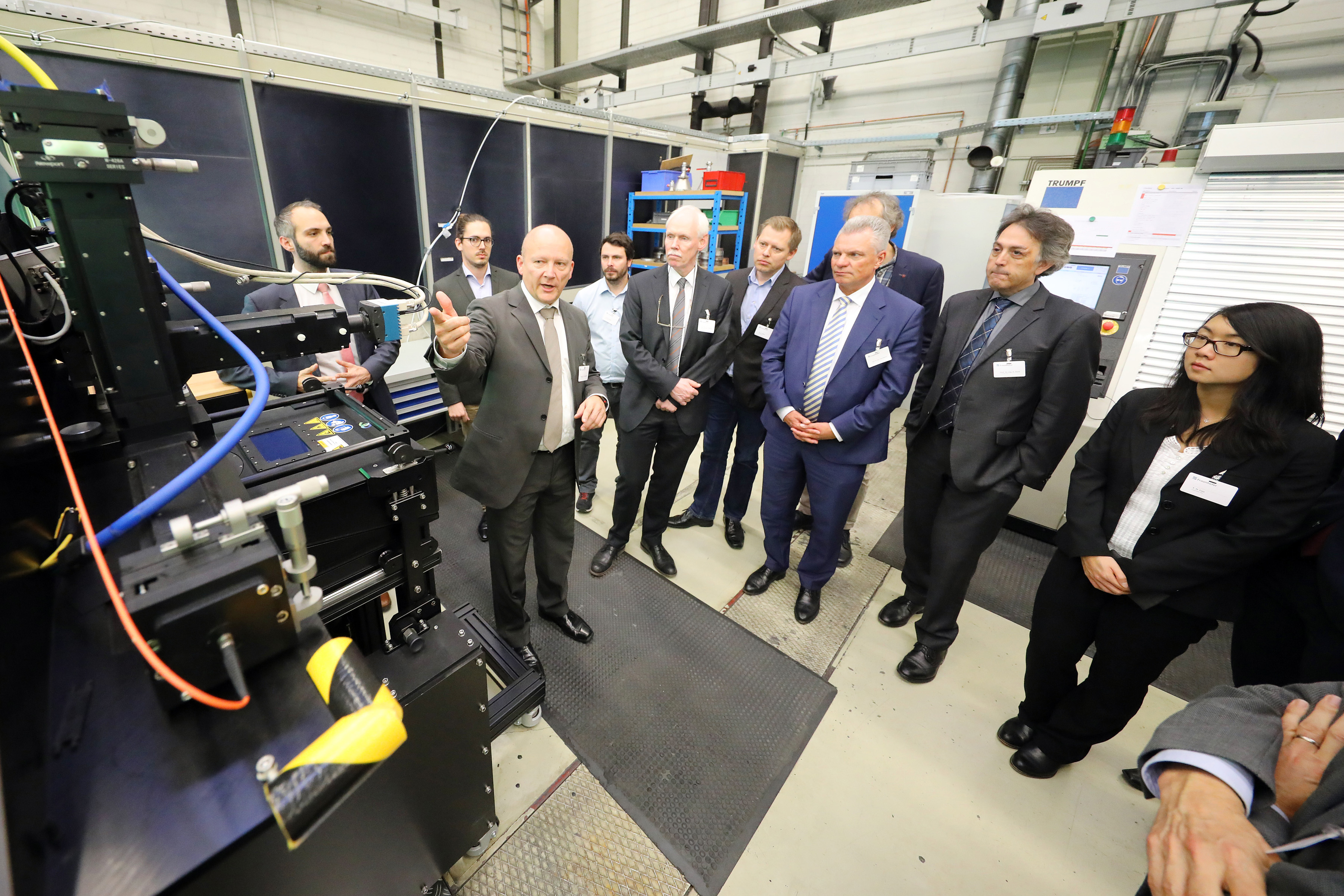 Teilnehmer des futureAM Kick-off Meetings bei der Laborführung am Fraunhofer ILT. Ulrich Thombansen erläutert die Systemtechnik zum Selektiven Laserschmelzen.