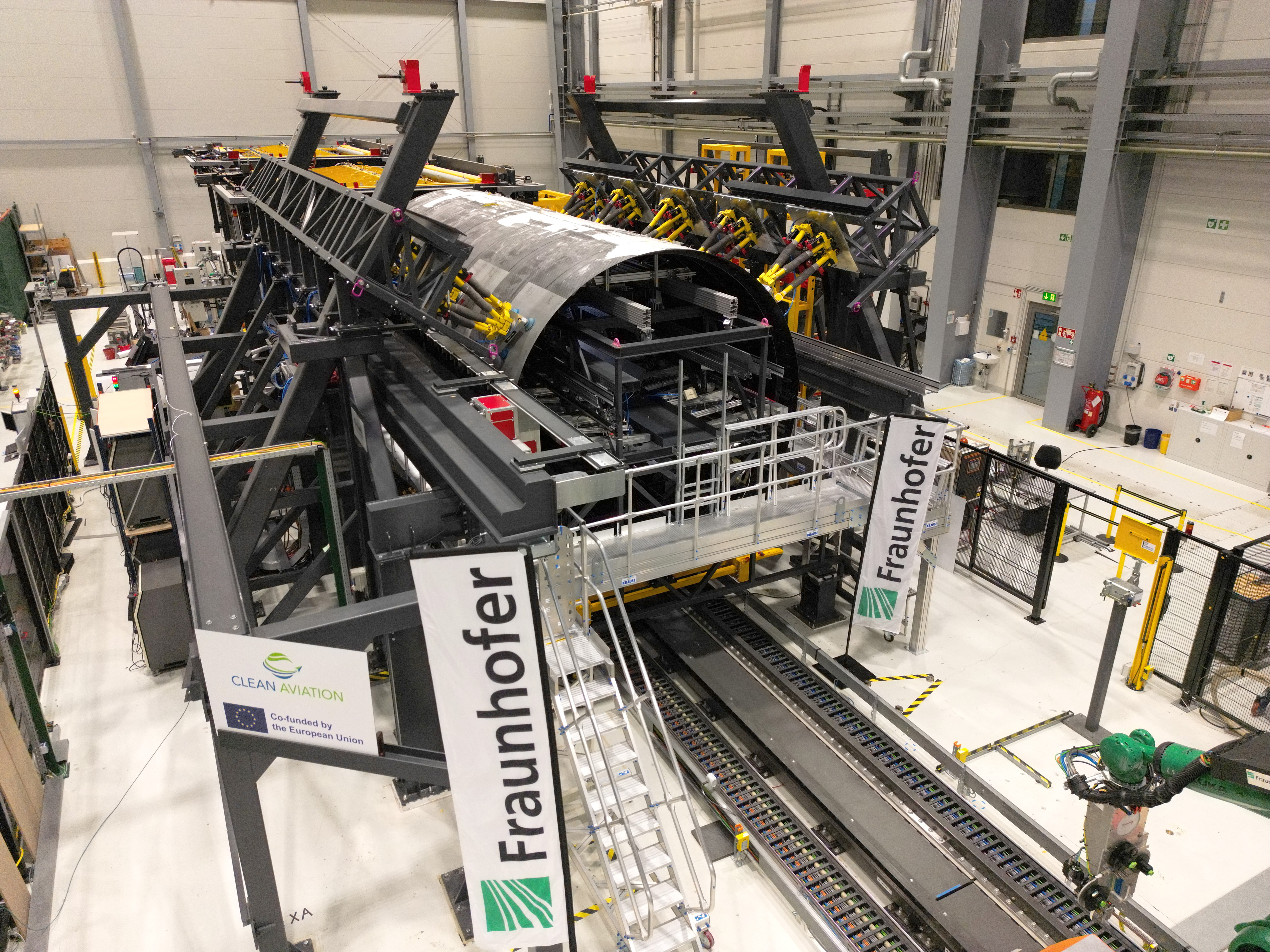 Montage-Forschungsplattform mit eingerüsteten thermoplastischen Rumpfschalen des »MFFD« bei der Fraunhofer-Gesellschaft in Stade. Gut erkennbar sind die gelben Hexapod-Roboter zum Halten und hochpräzisen Einstellen von Form sowie Lage der Oberschale.