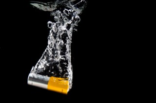 Alkaline AA battery falls with a splash into water on black background