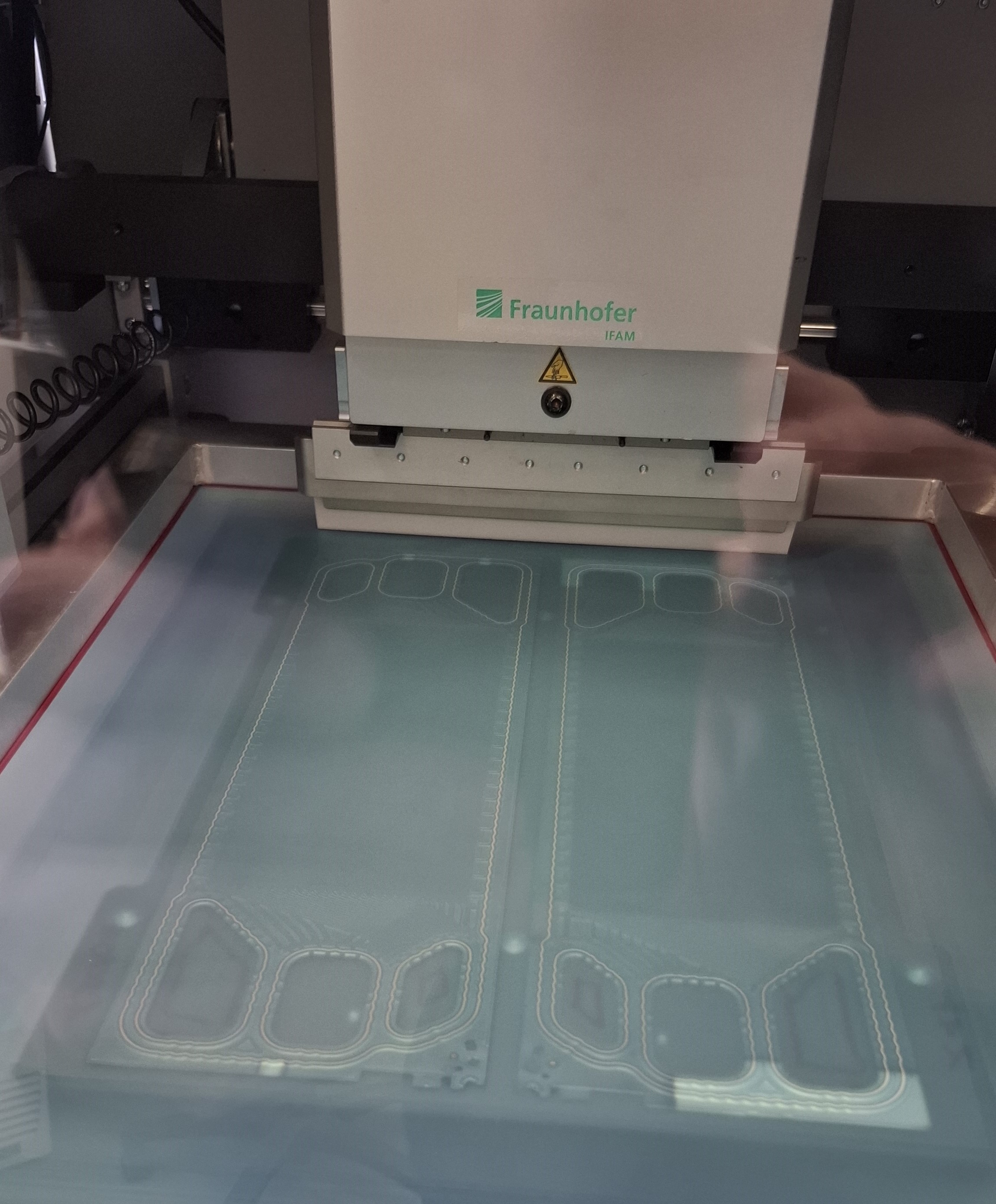 Bipolar plates are moved into the printing area fully automatically and the screen is aligned using register marks. The embossed metallic bead to be coated is clearly visible in the area of the media ports and along the outer edge of the bipolar plates. Bipolar plates are moved into the printing area fully automatically and the screen is aligned using register marks. The embossed metallic bead to be coated is clearly visible in the area of the media ports and along the outer edge of the bipolar plates.