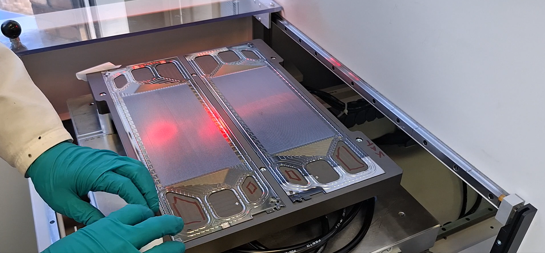 Bipolar plates from the ZSW are fixed in the printing nest using negative pressure. The structure of the printing nest and screen allow simultaneous coating on the anode (left) and cathode side (right) for each printing process. For printing on the reverse side, the bipolar plates are returned to the screen printing process after curing.
